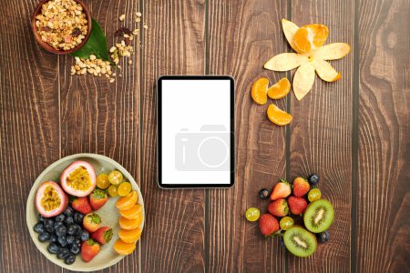 Photo for Tablet computer on wooden table next to plate with fresh fruits and granola bowl - Royalty Free Image