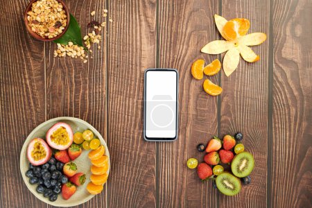 Foto de Smartphone en mesa de madera con frutas frescas y tazón de muesli - Imagen libre de derechos
