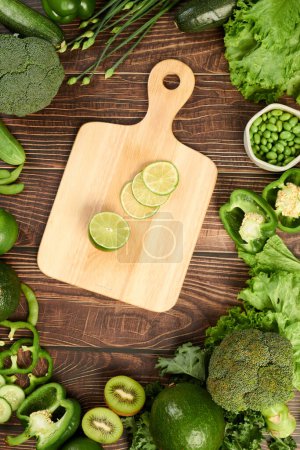 Photo for Cut lime on wooden board and green fruits and vegetables around, top view - Royalty Free Image