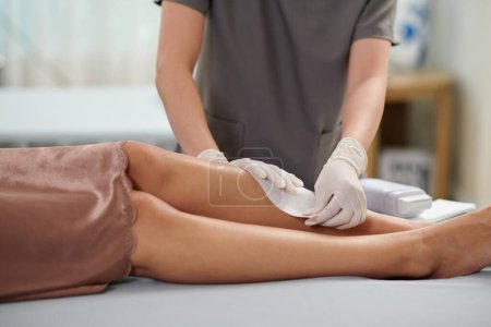 Photo for Cropped image of beautician removing paper strip when waxing legs of female client - Royalty Free Image