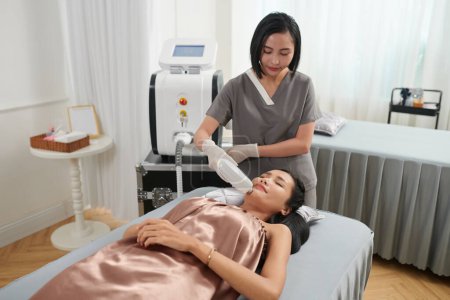 Téléchargez les photos : Esthéticienne clinique laser travaillant avec le client, enlever les cheveux sur le menton de la femme - en image libre de droit