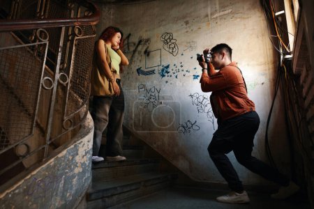 Téléchargez les photos : Jeune homme photographiant petite amie sur les marches dans le vieux bâtiment - en image libre de droit