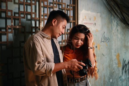 Photo for Vietnamese young man showing photos on screen of digital camera to girlfriend after shoot in old building - Royalty Free Image