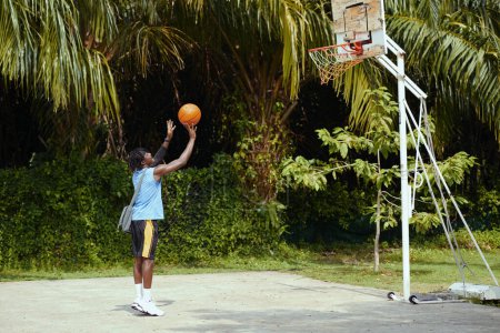 Téléchargez les photos : Homme noir jetant la balle dans le panier en jouant seul sur le terrain de basket - en image libre de droit