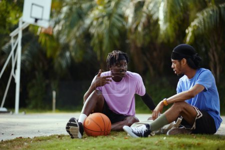 Photo for Friends sitting on ground in park and discussing game of streetball - Royalty Free Image