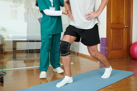 Foto de Hombre maduro con la pierna lesionada haciendo embestidas bajo control de fisioterapeuta - Imagen libre de derechos