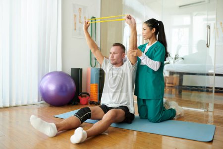 Foto de Terapeuta que controla al paciente manteniendo los brazos rectos cuando hace ejercicio con banda de resistencia - Imagen libre de derechos