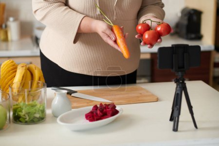 Foto de Mujer de talla grande mostrando ingredientes saludables de batidos vitamínicos al filmar el blog de cocina - Imagen libre de derechos