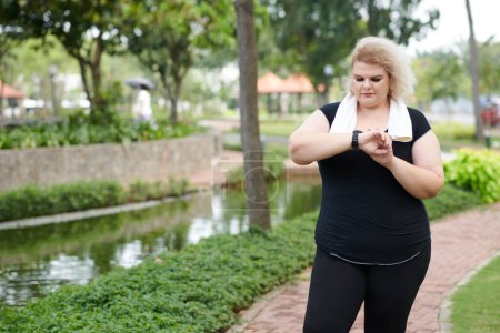 Téléchargez les photos : Plus la taille jeune femme vérifiant fitness tracker après avoir couru à l'extérieur - en image libre de droit