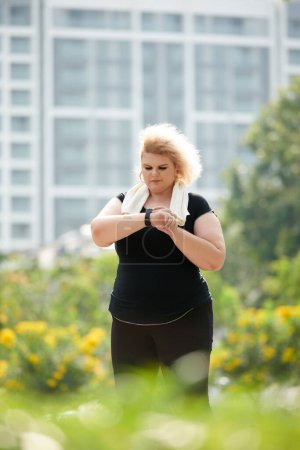 Téléchargez les photos : Curvy jogger vérifier la fréquence cardiaque sur le traqueur de fitness après l'entraînement - en image libre de droit