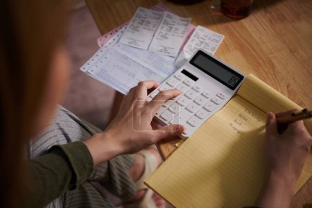 Téléchargez les photos : Femme calculant ses dépenses mensuelles et écrivant dans un carnet - en image libre de droit