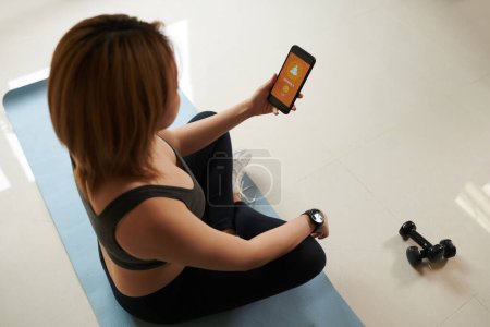 Photo for Young woman using mobile application when meditating at home - Royalty Free Image