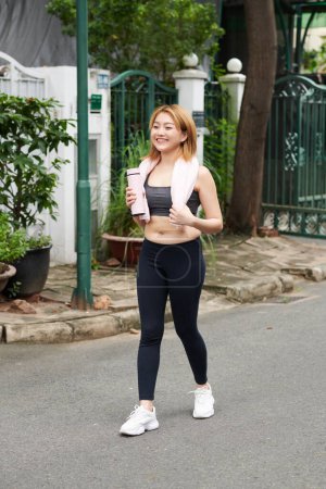 Téléchargez les photos : Joyeuse jeune femme asiatique marche à la maison après le jogging du matin - en image libre de droit