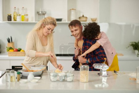 Foto de Mujer sonriente sirviendo pasta casera en platos para su marido y su hijo - Imagen libre de derechos