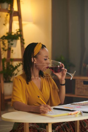 Téléchargez les photos : Illustrateur de mode créative boire un verre de vin rouge lors du dessin croquis - en image libre de droit