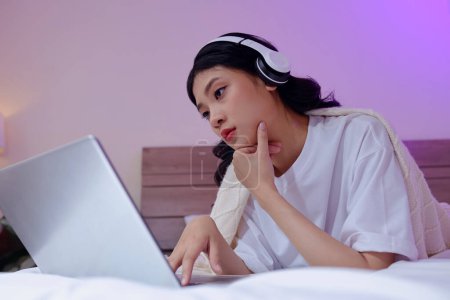 Téléchargez les photos : Jeune blogueur asiatique dans le casque d'édition vidéo sur ordinateur portable, ajoutant de la musique et des effets sonores - en image libre de droit