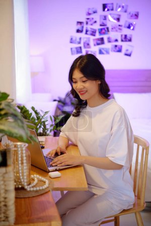 Téléchargez les photos : Souriant adolescente en coton t-shirt de travail sur ordinateur portable à la maison - en image libre de droit