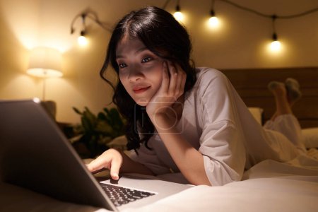 Photo for Asian teenage girl relaxing on bed and browsing the internet late at night - Royalty Free Image