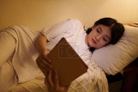 Téléchargez les photos : Adolescent fille lecture e-book dans lit tard dans la nuit - en image libre de droit
