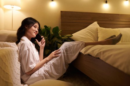 Foto de Sonriendo Asiática joven mujer en pijama llamando amigo o pareja - Imagen libre de derechos