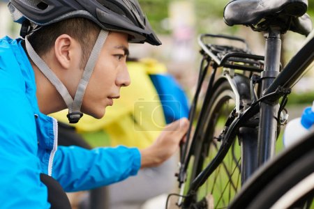 Téléchargez les photos : Cycliste fronçant les sourcils dans un casque de protection tuve vérifier les roues du vélo avant de monter - en image libre de droit