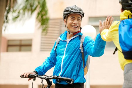 Photo for Joyful Vietnamese cyclist giving high five to friend after long ride in city - Royalty Free Image