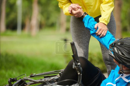Téléchargez les photos : Image recadrée de la femme aidant l'homme est tombé de vélo pour se lever - en image libre de droit