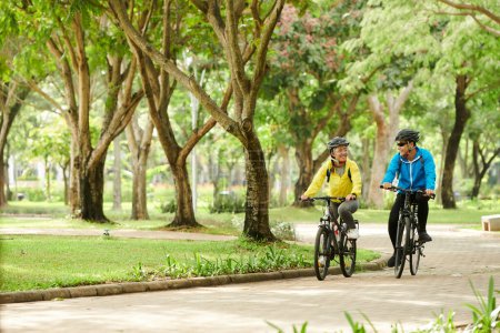 Photo for Happy boyfriend and girlfriend riding bicycles in city park when training for competition - Royalty Free Image