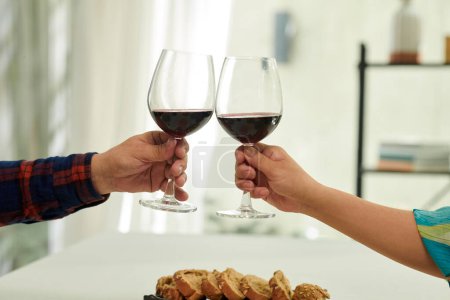 Photo for Hands of elderly couple toasting with glasses of red wine over dinner table - Royalty Free Image