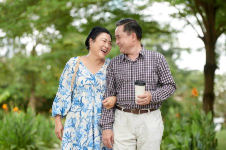 Téléchargez les photos : Femme âgée joyeuse riant à la blague du mari quand ils marchent dans le parc de la ville - en image libre de droit