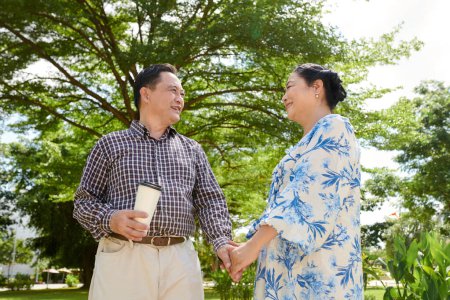 Photo for Happy senior couple holding hands when walking in park on sunny day - Royalty Free Image