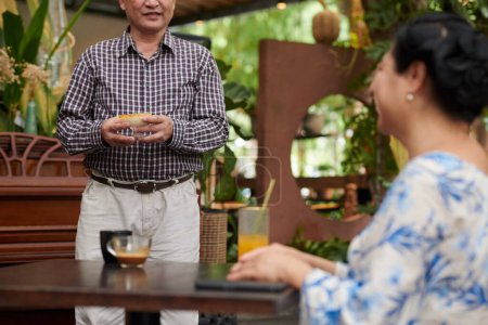 Téléchargez les photos : Senior homme apportant désert à sa femme assise à la table du café - en image libre de droit