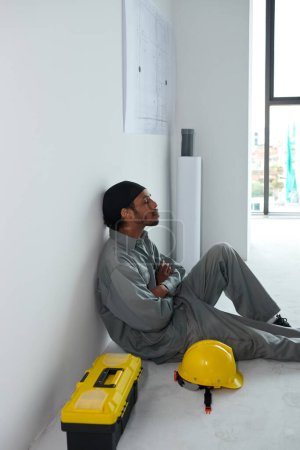 Téléchargez les photos : Constructeur fatigué appuyé sur le mur lors du repos pendant une courte pause sur le chantier de construction - en image libre de droit