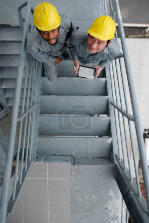 Téléchargez les photos : Constructeurs en hardhats monter les escaliers et regarder la caméra - en image libre de droit
