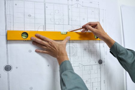 Manos del constructor utilizando el nivel de construcción al medir la línea en el plan de construcción