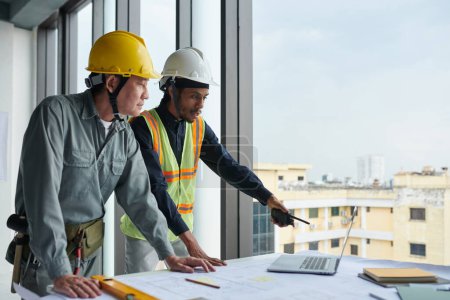 Foto de Trabajadores de la construcción mirando el gráfico en la pantalla del ordenador portátil al discutir el plan de construcción - Imagen libre de derechos