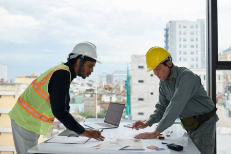 Foto de Ingeniero y trabajador de la construcción inclinándose sobre la mesa con planos - Imagen libre de derechos