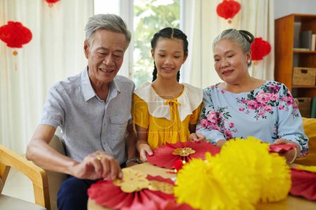 Photo for Grandparents teaching girl how to make red and yellow paper decorations for Tet - Royalty Free Image
