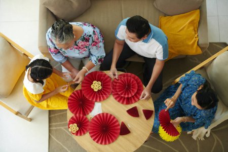 Téléchargez les photos : Famille réunie à la maison pour faire des décorations de vacances Tet en papier rouge et jaune, vue sur le dessus - en image libre de droit
