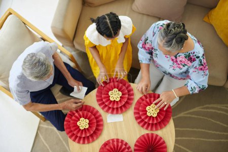 Photo for Teenage girl and granddaughter making paper decorations for Tet celebration, top view - Royalty Free Image