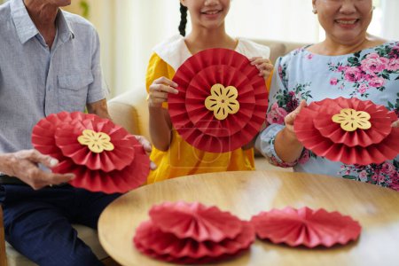 Téléchargez les photos : Joyeuse adolescente et ses grands-parents faisant des décorations traditionnelles en papier pour les vacances au Tet - en image libre de droit