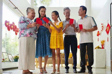 Téléchargez les photos : Membres excités de la famille échangeant des enveloppes d'argent chanceux lors de la célébration du Tet - en image libre de droit