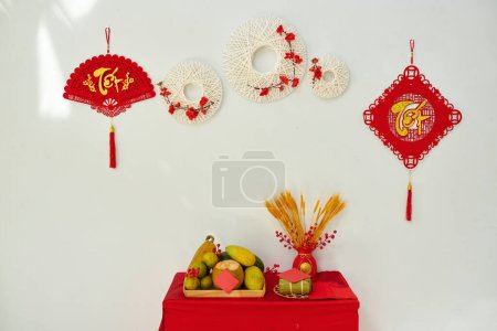Téléchargez les photos : Nouvel an lunaire vietnamien décorations avec des ornements suspendus sur le mur et la table avec des fruits frais - en image libre de droit