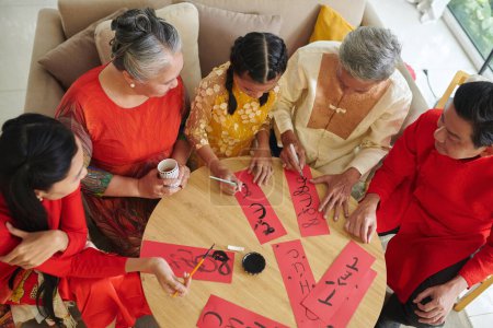 Téléchargez les photos : Couplets d'écriture de famille sur feuille de papier rouge lors de la préparation pour les célébrations du Tet - en image libre de droit