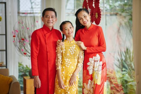 Téléchargez les photos : Les parents souriants et leur fille adolescente portant des costumes traditionnels lors de la célébration Tet à la maison - en image libre de droit