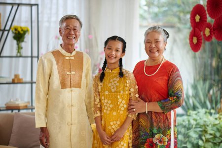Téléchargez les photos : Portrait de grands-parents heureux et de leur petite-fille adolescente portant des costumes traditionnels Tet - en image libre de droit