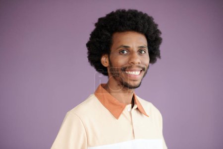 Téléchargez les photos : Portrait studio de l'homme noir excité debout sur fond lilas et souriant à la caméra - en image libre de droit