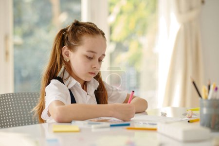 Photo for Creative schoolgirl drawing in textbook at school desk - Royalty Free Image