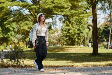 Téléchargez les photos : Joyeux adolescent fille avec planche à roulettes marche sur le campus après les cours - en image libre de droit