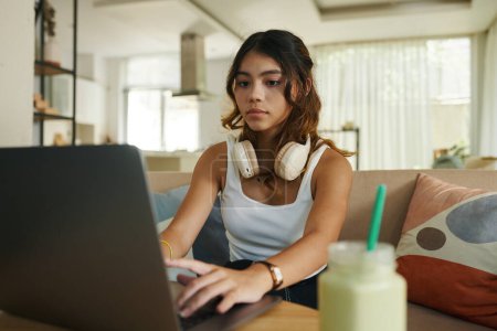 Foto de Chica adolescente seria con auriculares que trabajan en el ordenador portátil - Imagen libre de derechos